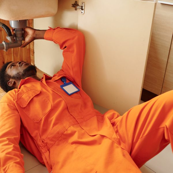 Professional plumber installing or fixing plastic pipe under kitchen sink in house of customer